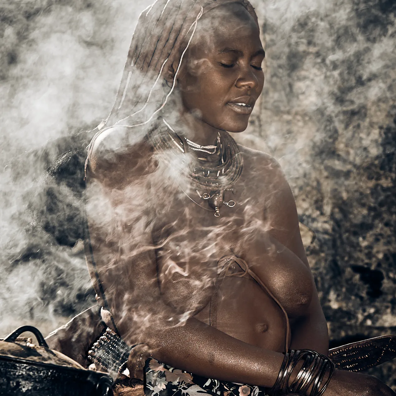 A cultural study of a Himba woman beside a fire, documenting the warmth and enduring heritage of Namibia's ancestral guardians.