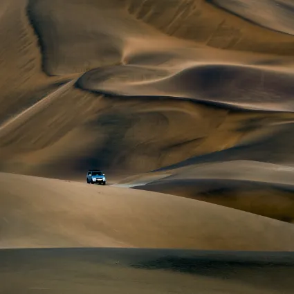 A structural study of an expedition vehicle navigating the unyielding dune sea of the Namib; documenting the logistical precision and native expertise required to access the vanishing realms.