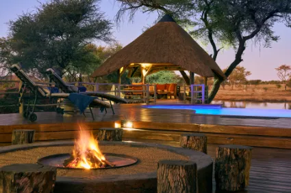 A dusk study of the Villa's infinity pool and firepit, where the warmth of the hearth meets the cooling blue hour of the Okonjima Nature Reserve.