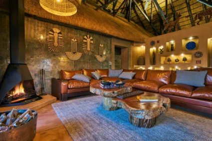 The interior lounge of the African Villa, showcasing the 'safari-chic' blend of leather, stone, and traditional artefacts anchored by a central fireplace.