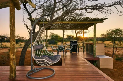 The private timber deck of a Kalenga safari tent, offering an elevated perspective over the red Kalahari sands and Camel-thorn canopy.