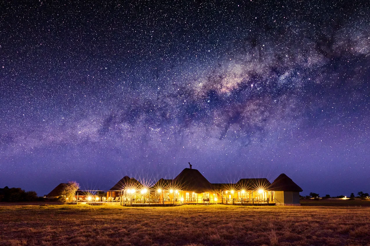 The central lodge architecture at Kalahari Red Dunes, featuring expansive timber decks that overlook the natural vlei and watering hole.