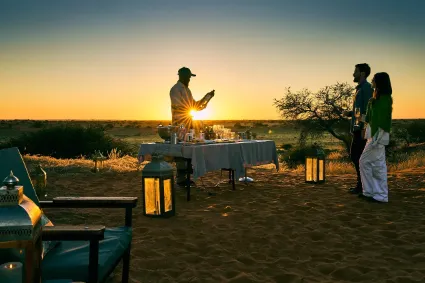 A guided sundowner experience atop the red dunes, capturing the authentic human connection to the land at the close of the day.