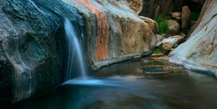 A mountain stream cascading over smooth granite bedrock, illustrating the persistent flow of the desert's secretive water sources.