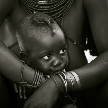 A young Himba child seeking comfort from his mother, illustrating the close-knit familial bonds of the nomadic northern tribes.