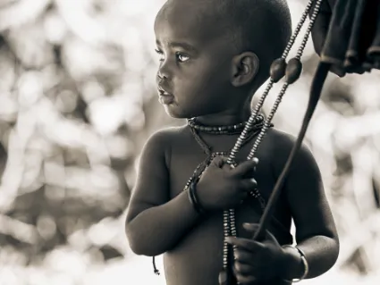 A Himba child clinging to his mother, a study of the secure and tangible human connections found within the traditional family unit.