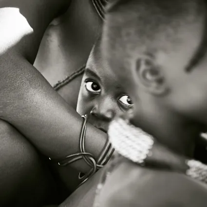 A shy Himba child clutching his mother's arm, capturing a quiet, private moment amidst the vastness of the Kaokoland landscape.
