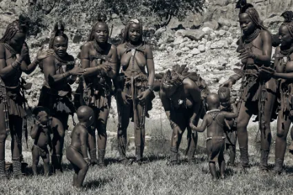 A group of Himba women and their children engaged in a communal dance, showcasing the joy and collective spirit of the village.