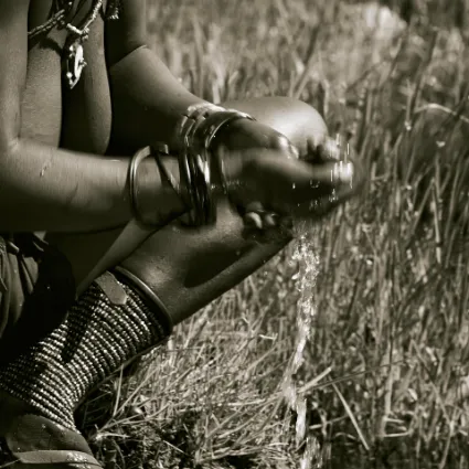 A Himba woman washing her hands in the clear water of a natural spring, documenting the vital relationship between the tribe and the land's hidden water veins.