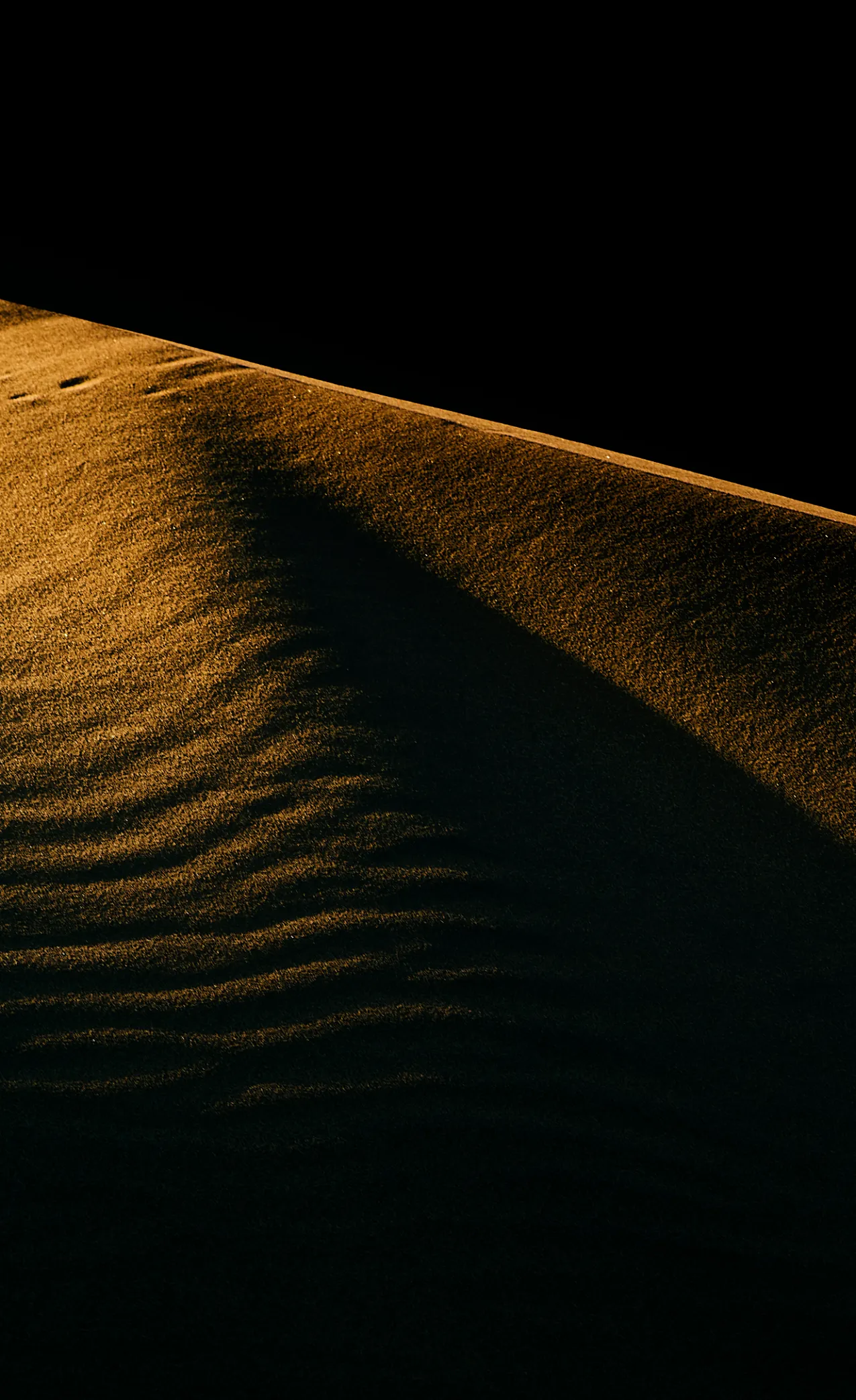 A minimalist abstract study of a Namibian sand dune, where the final light of day accentuates the undulating ridges and rhythmic textures of the desert.