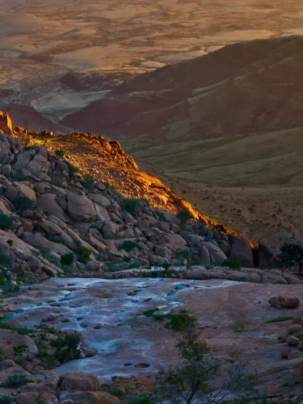 An ethereal study of the Amis Gorge after rare rainfall, where fleeting water pools reflect the evening light over the western Brandberg and coastal plains.