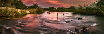 The Kavango River flowing over Popa Falls at sunset, documenting the lush, riverine veins of Namibia's northern reaches.