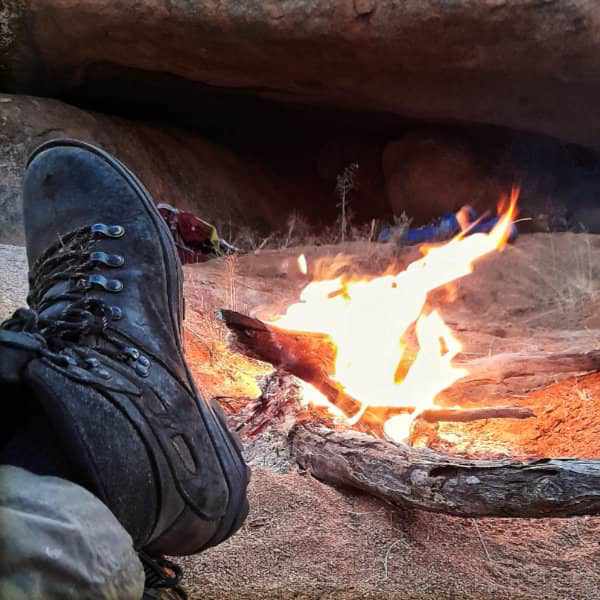 Sturdy outdoor boots by a campfire, set against a backdrop of wilderness, capturing the essence of adventure and solitude