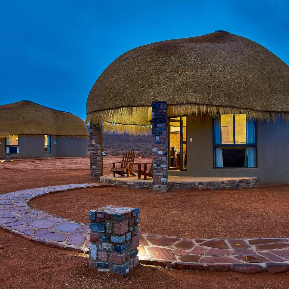 Unique circular thatched-roof building at Wekibi Lodge, showcasing traditional Namibian architecture with modern glass elements at dusk.