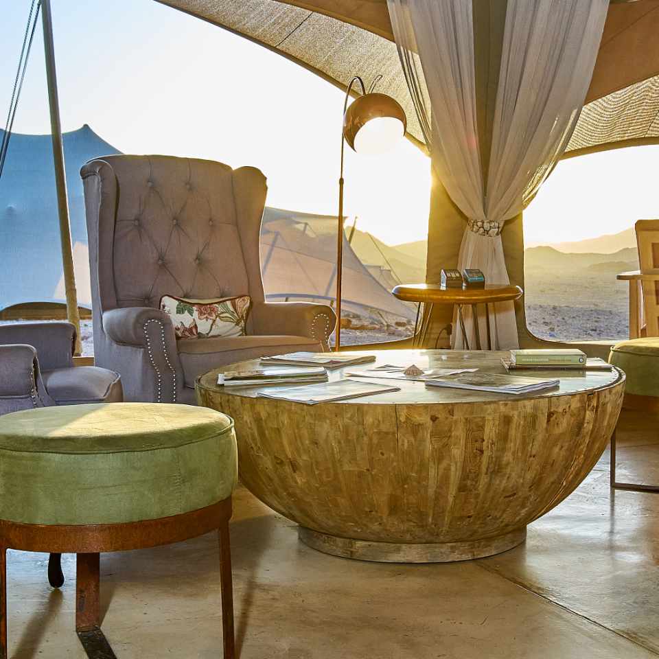 Luxurious lounging area at Desert Hills Glamping Camp, Sossusvlei, with plush armchair, elegant decor, and panoramic desert views at sunset.