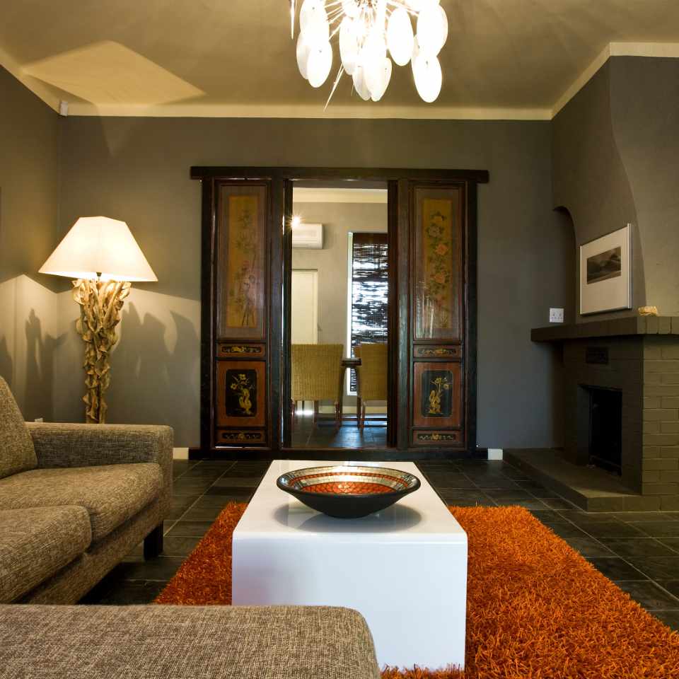 Chic and modern living room at a guesthouse in Omaruru, featuring a plush grey sofa, unique lighting, and elegant double doors leading to a sunlit room.