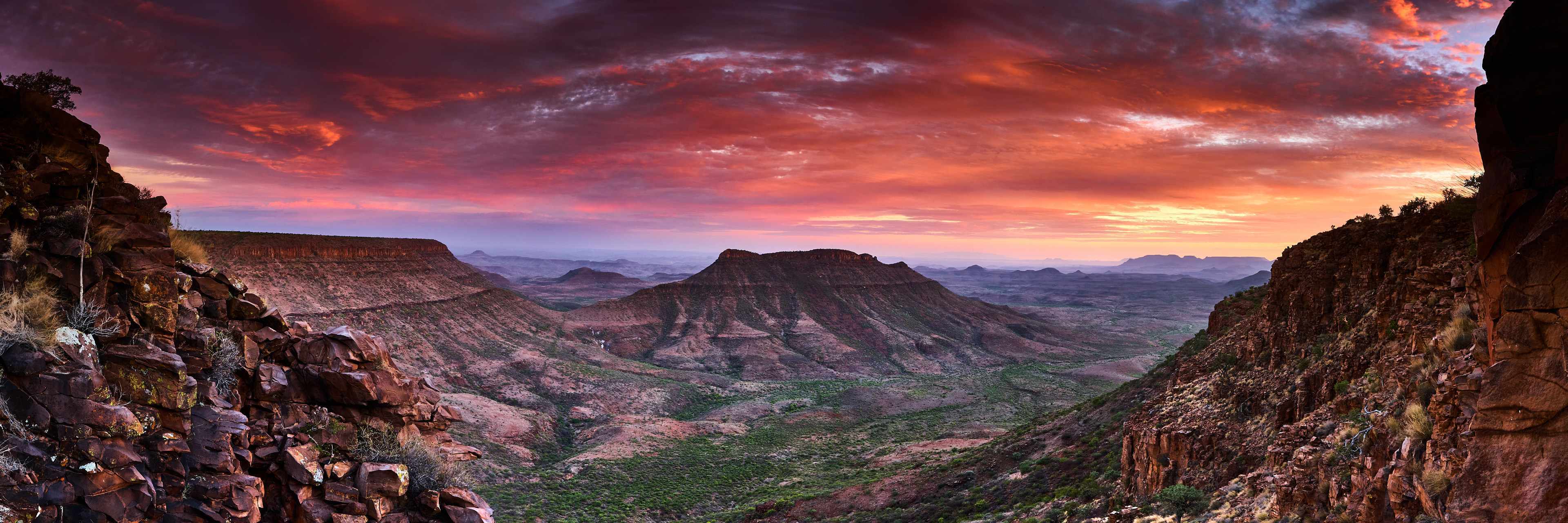 Panoramic sunset view of Klip River Valley from Grootberg Lodge, featuring jagged cliffs and a lush green ecosystem under a vibrant dusk sky.