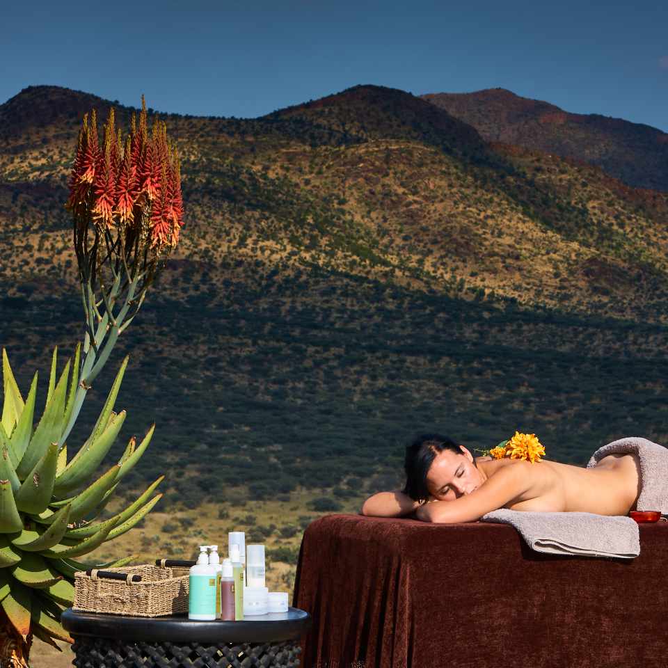 Serene outdoor massage setup at GochaGanas Lodge, Namibia, with a backdrop of lush mountains and clear skies, featuring a massage table and natural aloe plant.