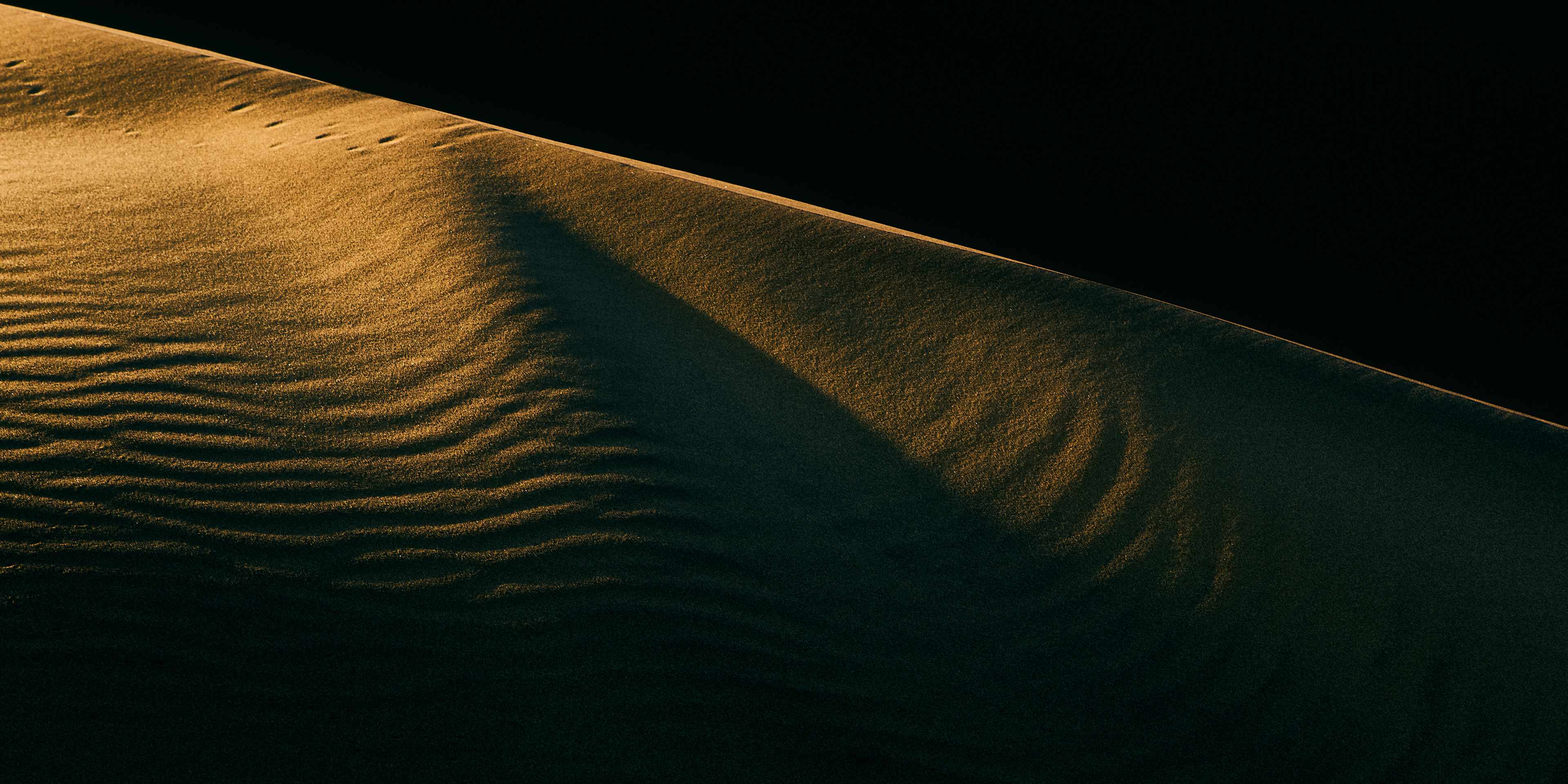 Sunset enhanced abstract: The setting sun clips the tip of a dune in the heart of the Namib Desert, casting an ethereal glow over the abstract pattern of sand ripples, capturing the serene beauty of this vast wilderness