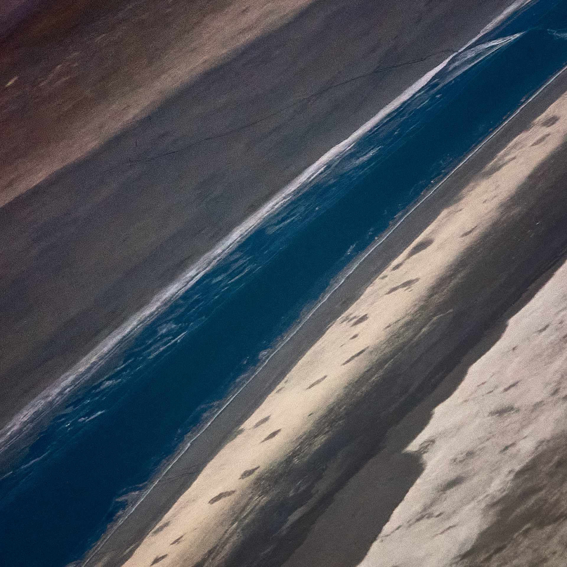 Aerial view of Etosha Pan showcasing the striking contrast of dark moist clay against the lighter dry clay pan, with a distinctive blue streak indicative of water, highlighting the abstract beauty of Namibia's natural patterns and gradients.