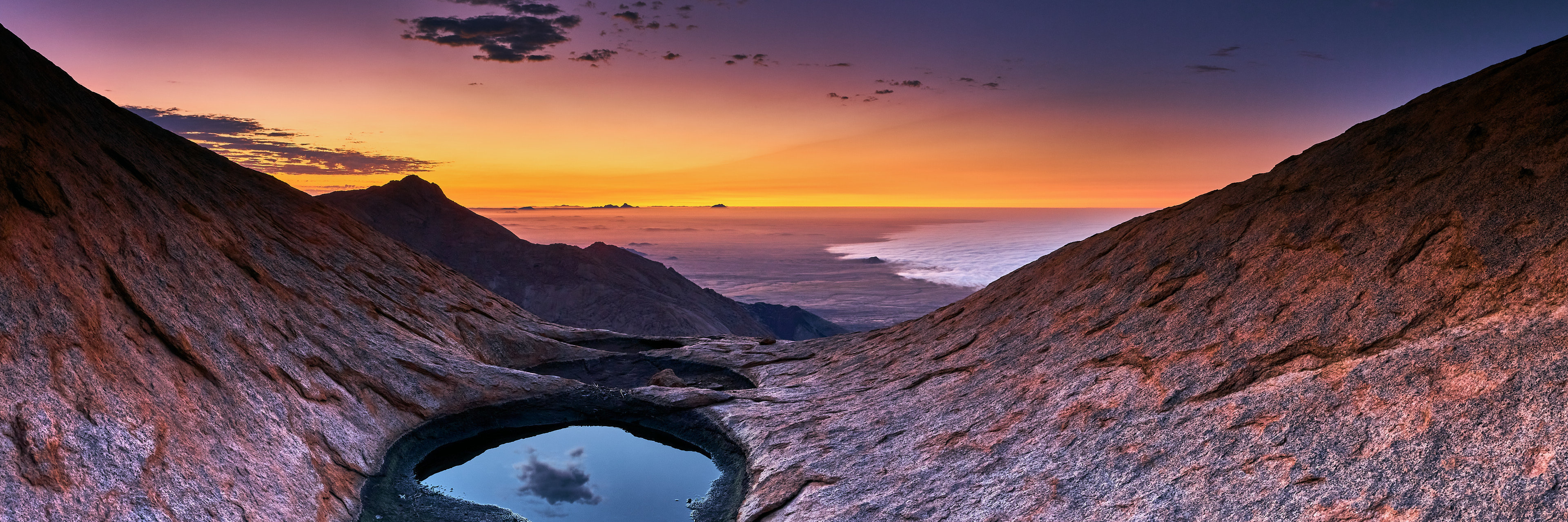 Brandberg Vista: A breathtaking panoramic view from atop Brandberg, capturing the distant silhouette of Spitzkoppe against the horizon, the ethereal mist rolling in from the Atlantic Ocean, and the unique landscape of the Hungorob Platen.