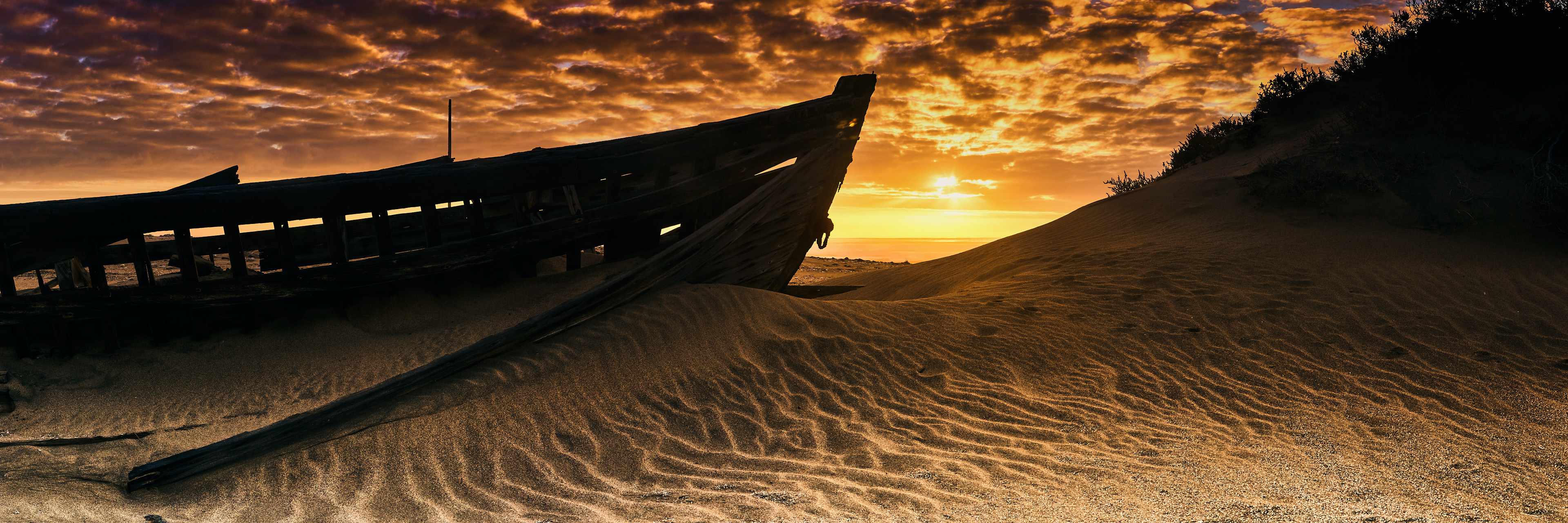 Abandoned whaling ship wreck on Namibia's Skeleton Coast, captured at sunset with vibrant sky colors reflecting over golden sands, symbolizing nature's reclaiming of human artifacts.