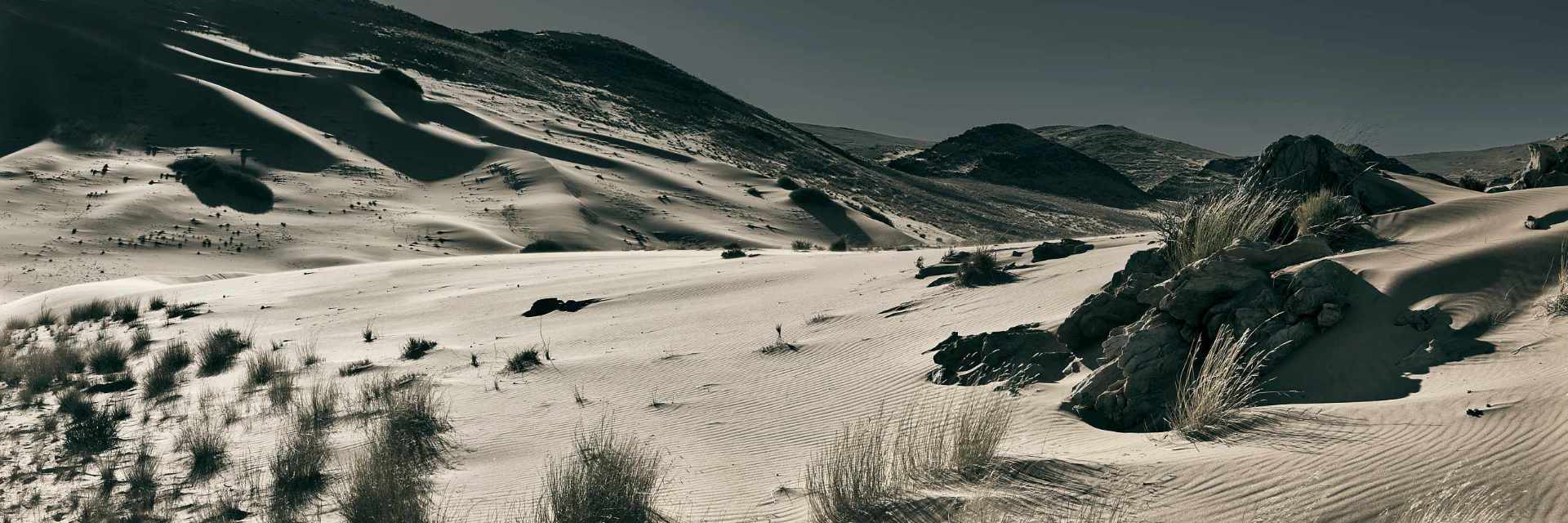 Stark photograph of dunes engulfing Hartmann's Mountain in Northern Namibia, showcasing the dramatic desert landscape.