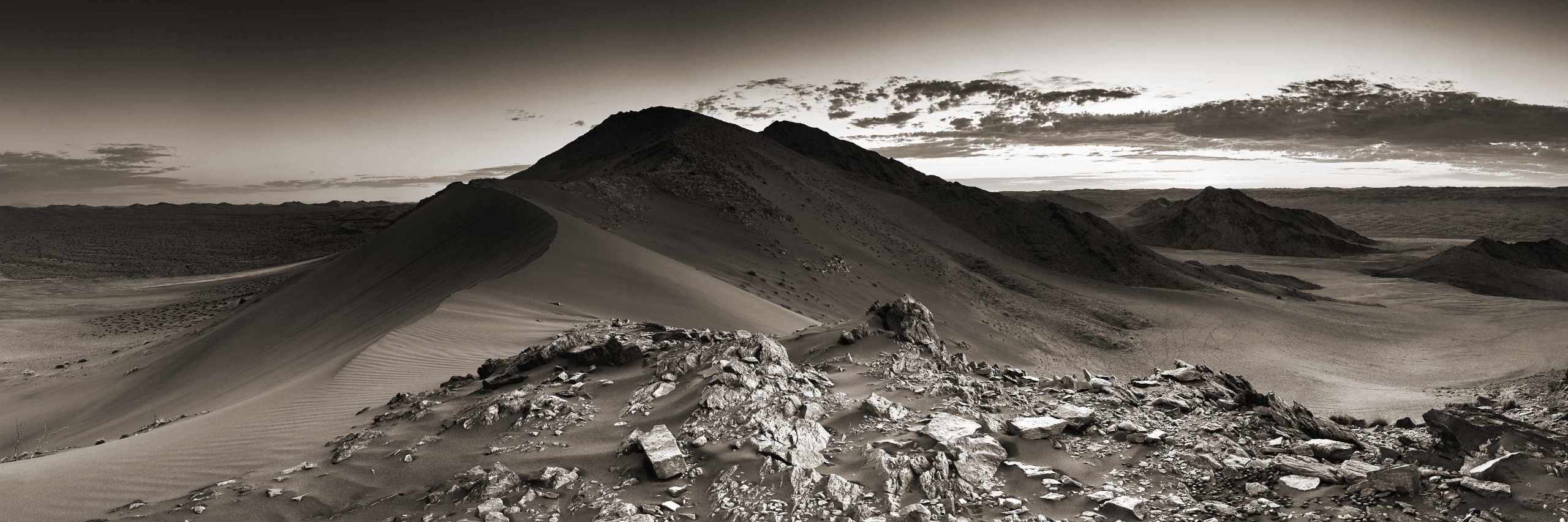 Sepia-toned image capturing the stark beauty of White Mountain, a prominent rocky outcrop rising from the dunes south of Deadvlei in Namibia's Namib-Naukluft Park.