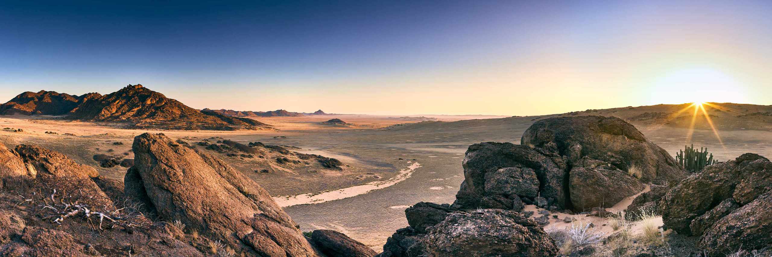 
            unset Over Hartmans Mountain: A breathtaking view from Hartmans Mountain in Northern Namibia, capturing the moment the sun touches the horizon, creating a stunning sun star effect. The image overlooks the vast dunes to the west and mountains to the east, encapsulating the diverse and majestic landscapes of Namibia